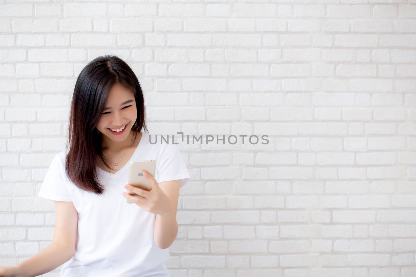 Beautiful of portrait young asian woman touch phone and smile standing on cement brick background, freelance female calling telephone, communication concept.