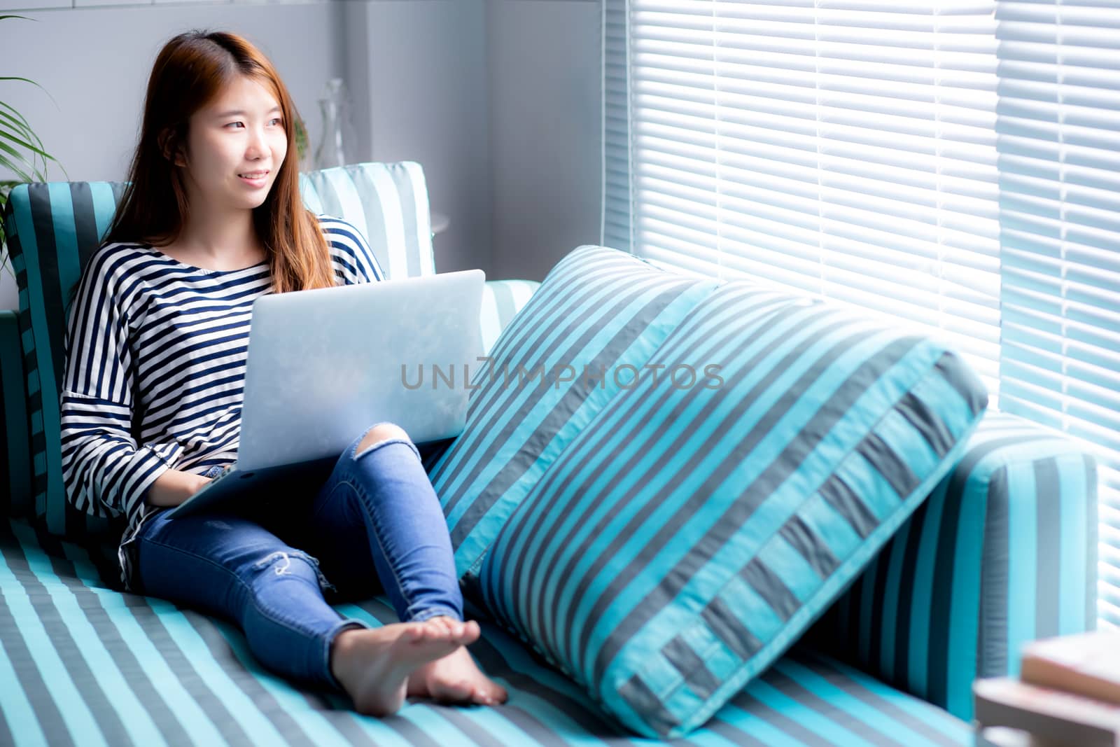 Beautiful of portrait young asian woman using laptop for leisure on sofa in living room, girl working online with notebook freelance with a happy, communication business concept.