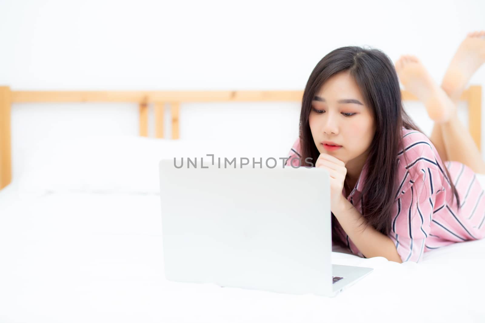 Beautiful asian young woman lying on bed using laptop at bedroom for leisure and relax, freelance with girl working notebook, communication concept.