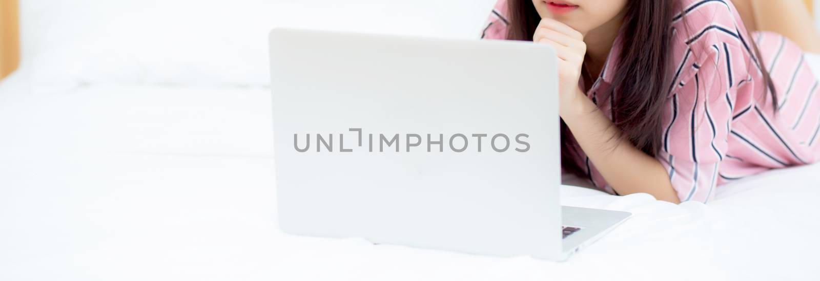 Banner website asian young woman lying on bed using laptop at bedroom for leisure and relax, freelance with girl working notebook, communication concept.