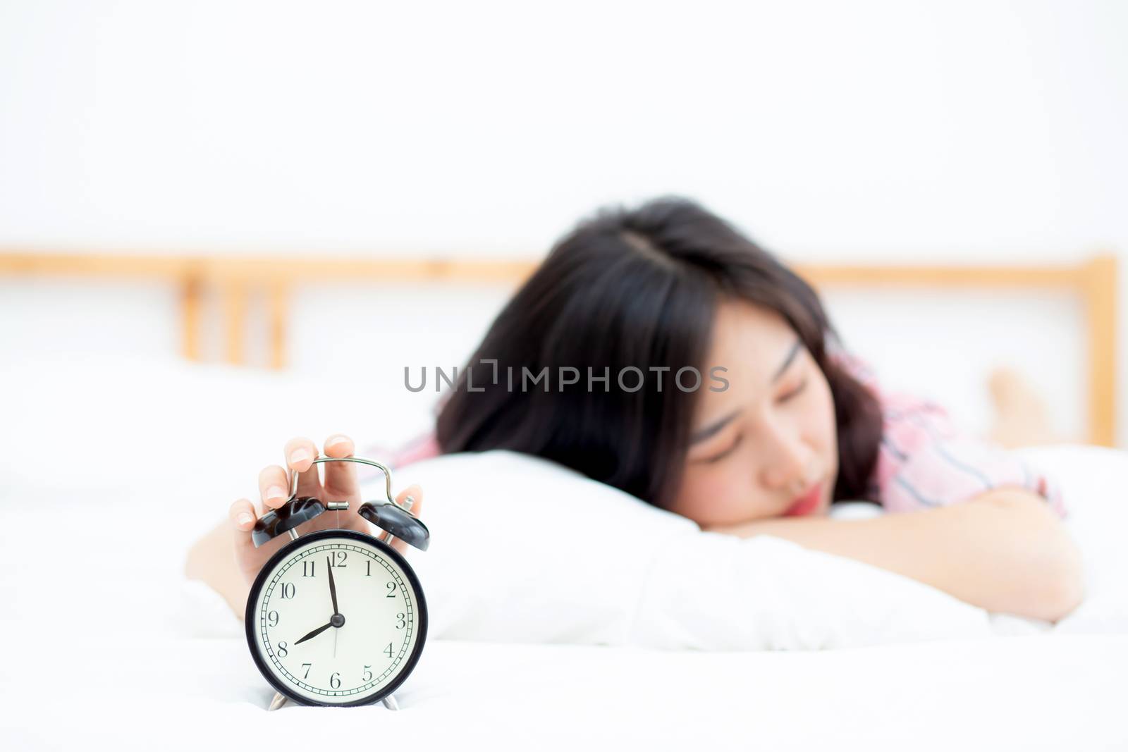 Beautiful asian young woman turn off alarm clock in morning, wake up for sleep with alarm clock, relax and lifestyle concept.