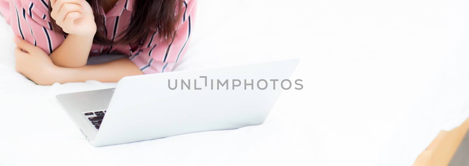 Banner website asian young woman lying on bed using laptop computer at bedroom for leisure and relax, freelance with girl working notebook, communication and lifestyle concept.
