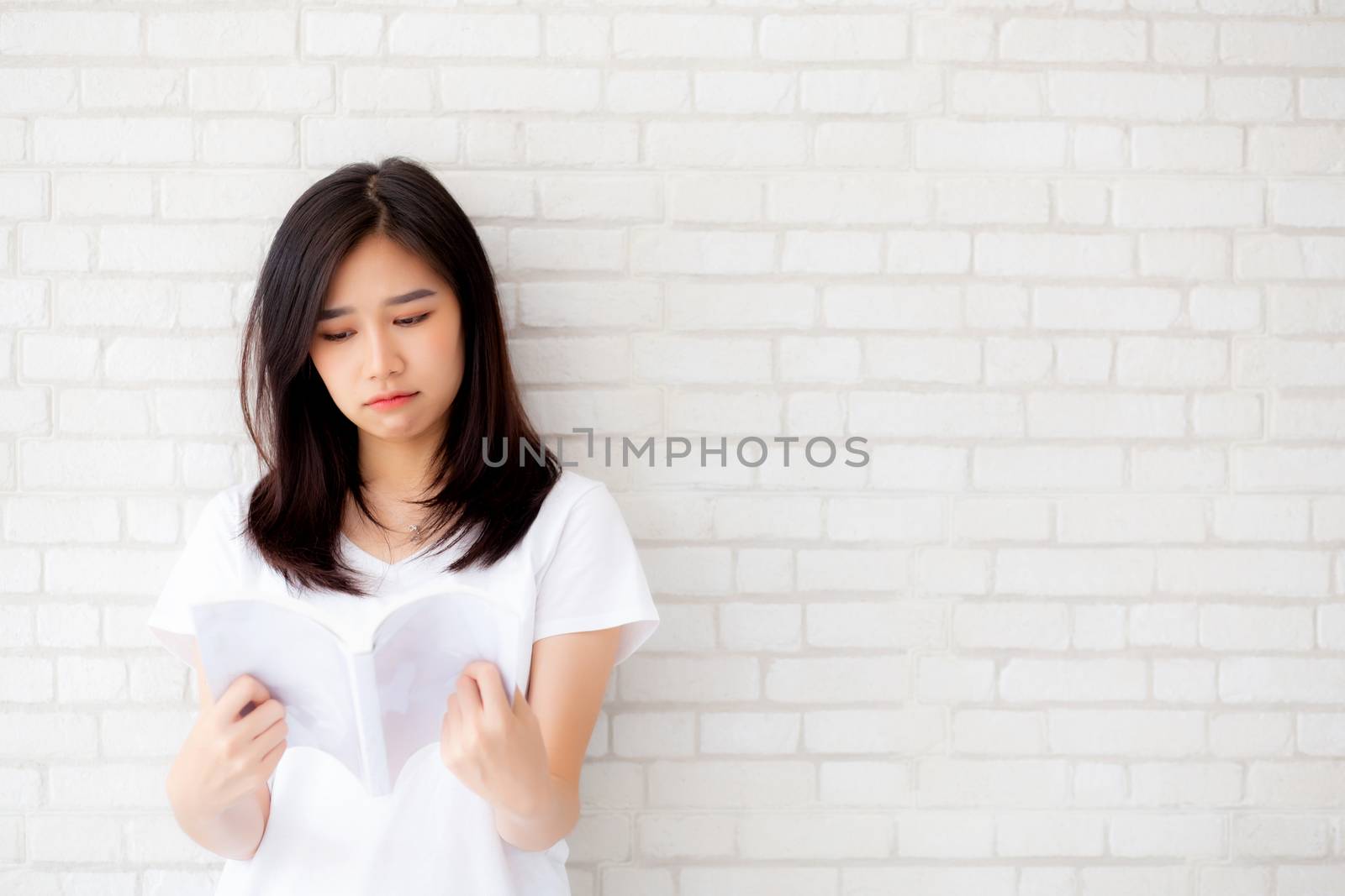 Beautiful of portrait young asian woman happiness relax standing reading book on concrete cement white background at home, girl happy study content literature, education and lifestyle concept.