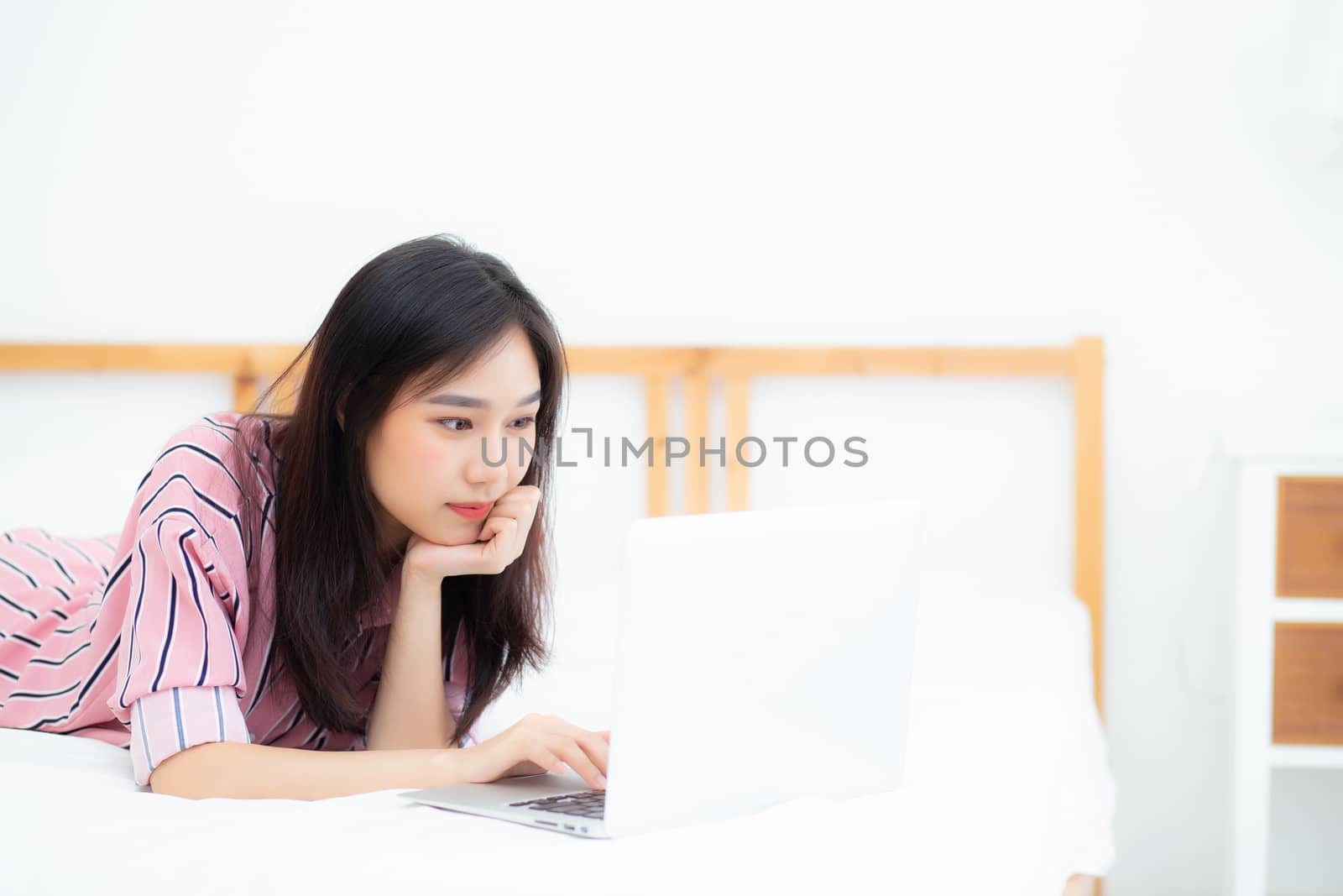 Beautiful asian young woman lying on bed using laptop at bedroom by nnudoo