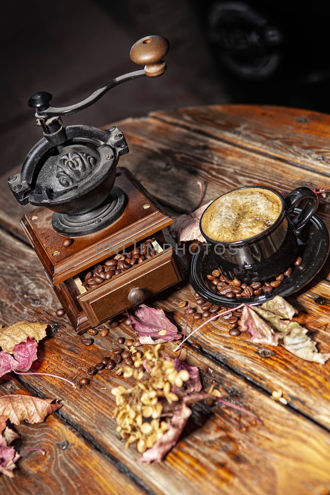 Coffee mill, beans, cup of coffee and autumn leaves on a wooden desk