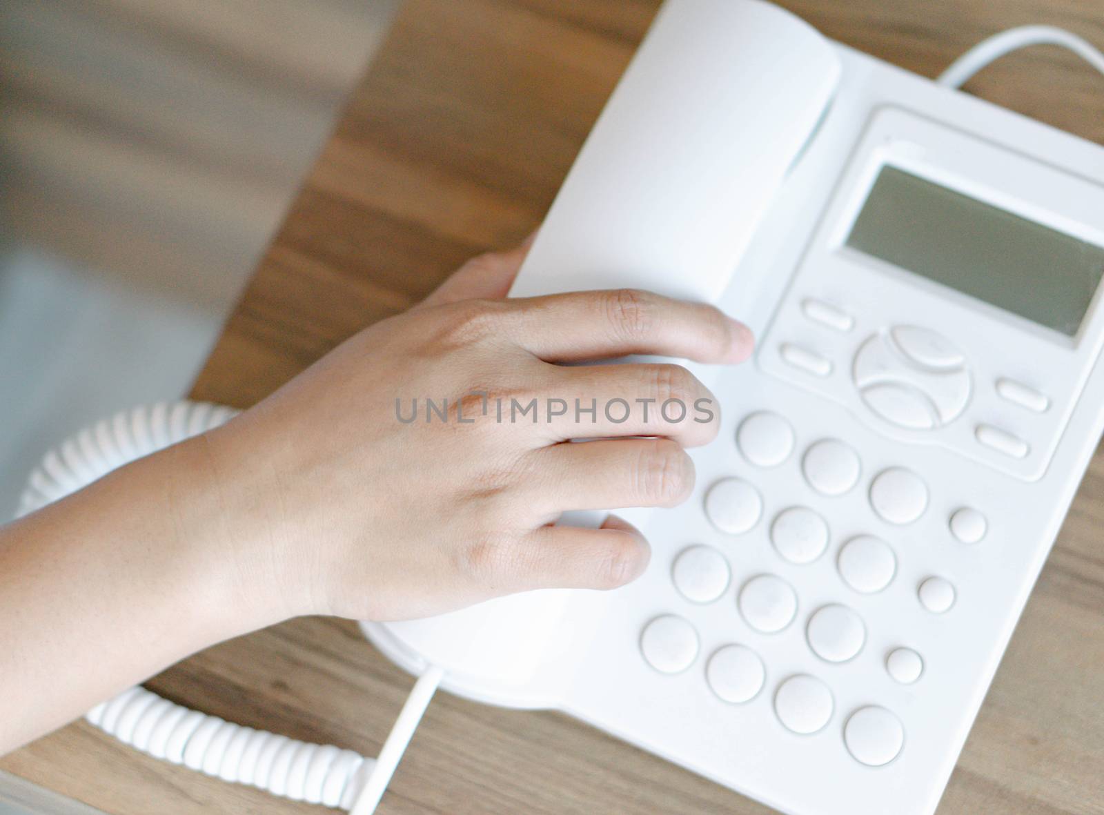 Closeup woman hand holding telephone receiver and dialing a phone number on white landline telephone.