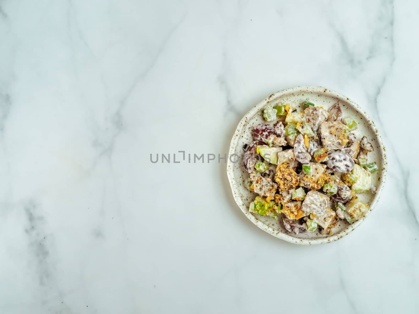 Waldorf salad with copy space. American fruit and nut salad with apples, celery, grapes, chicken meat, dressed mayonnaise. Craft plate with ready-to-eat waldorf salad on white marble. Top view