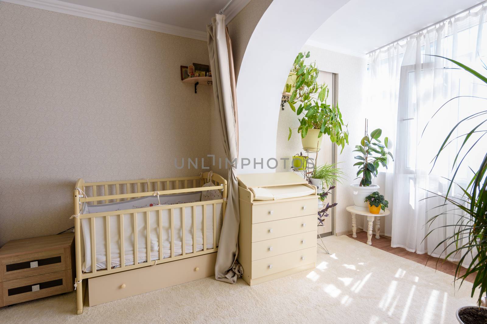 A newborn baby's crib and a changing table stand at the entrance to the glazed balcony