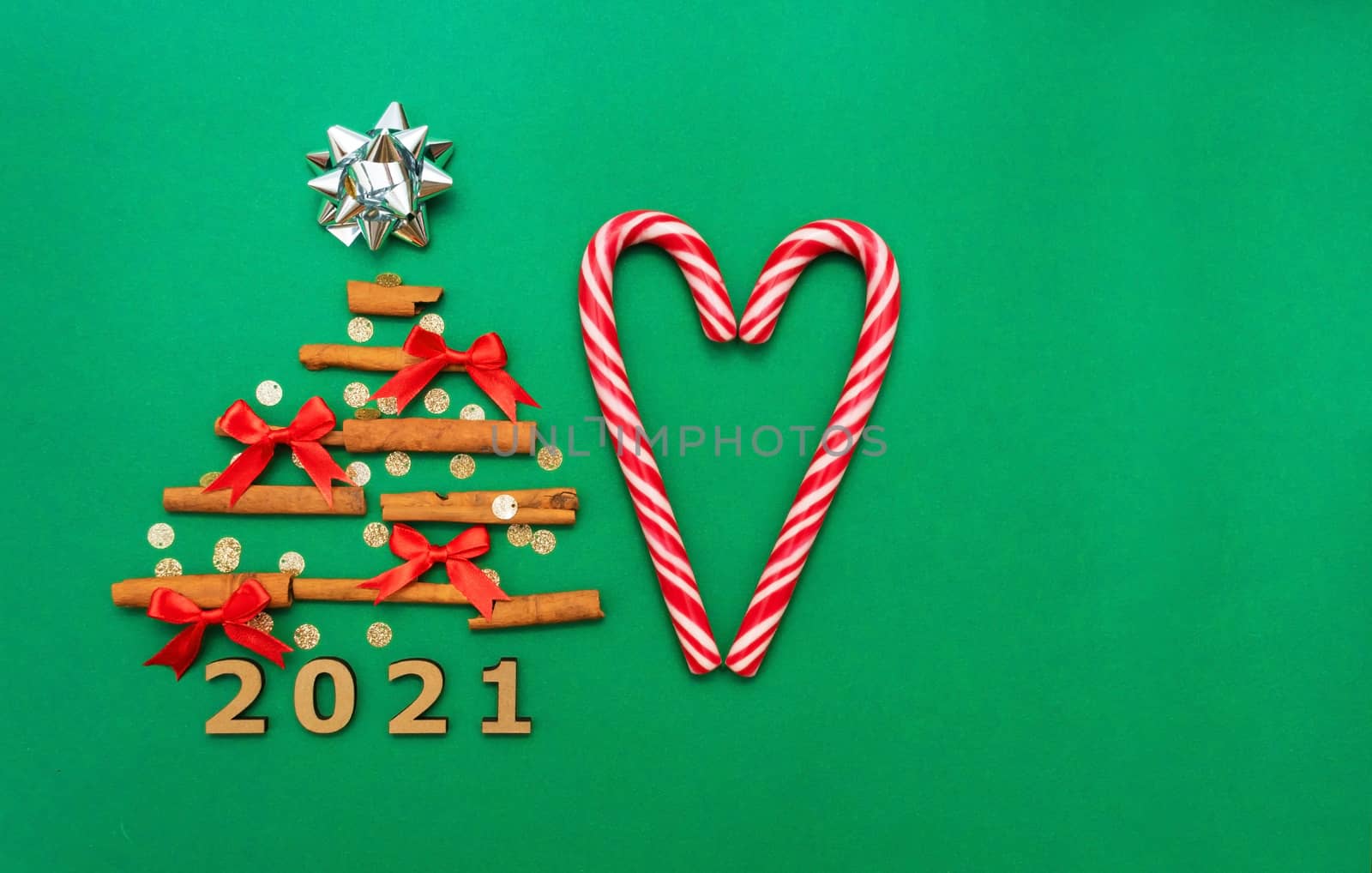 Christmas composition 2021 cinnamon tree, red bows, candy, Christmas cane candies on a green background. Christmas, winter, new year concept. Flat lay, top view, copy space by Alla_Morozova93