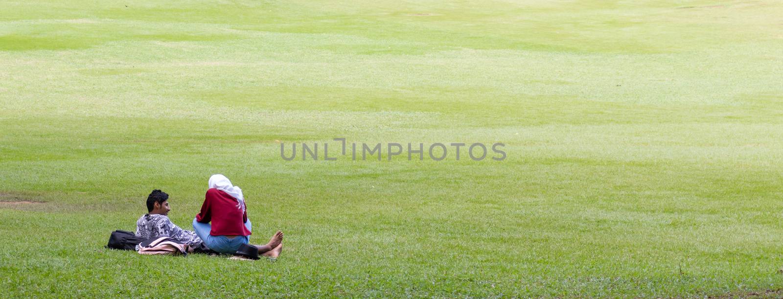 Young Couple Relaxing in Victoria park grass field. by nilanka