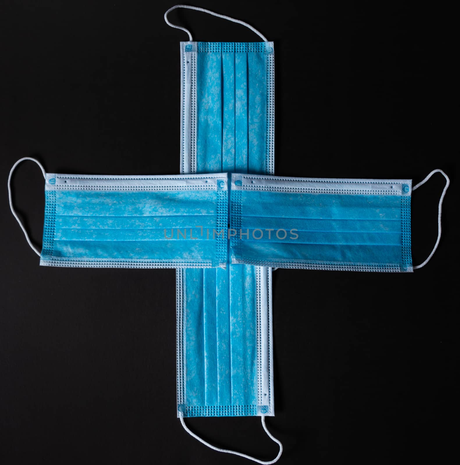 Four surgical face masks put together as a cross in black background