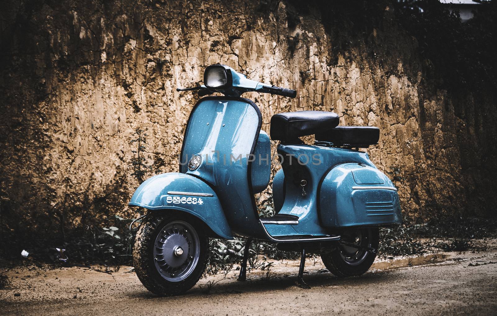 Vintage light blueish scooter bike against dirt wall by nilanka