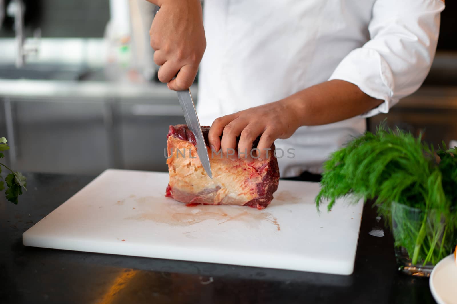 unrecognizable young African chef standing in professional kitchen in restaurant preparing a meal of meat and cheese vegetables. Portrait of man in cook uniform Cuts meat with a metal knife.