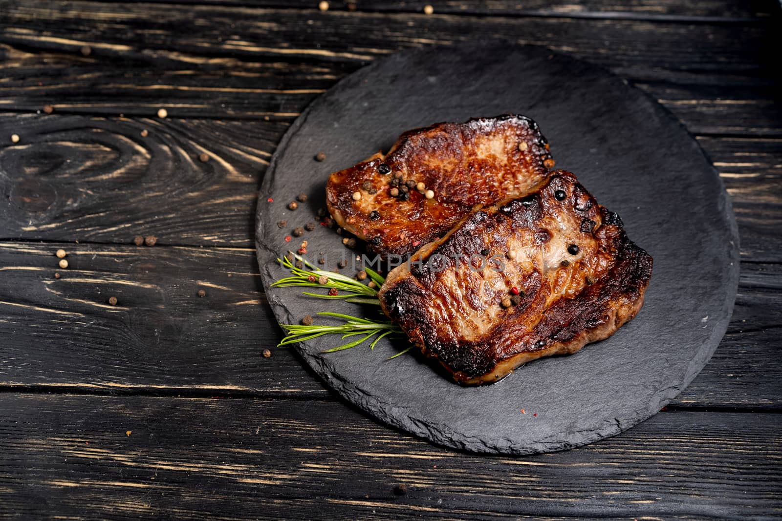 A juicy piece of fried meat lies on a stone plate against a black wooden table. Degree of roasting well done. Food concept with copy space