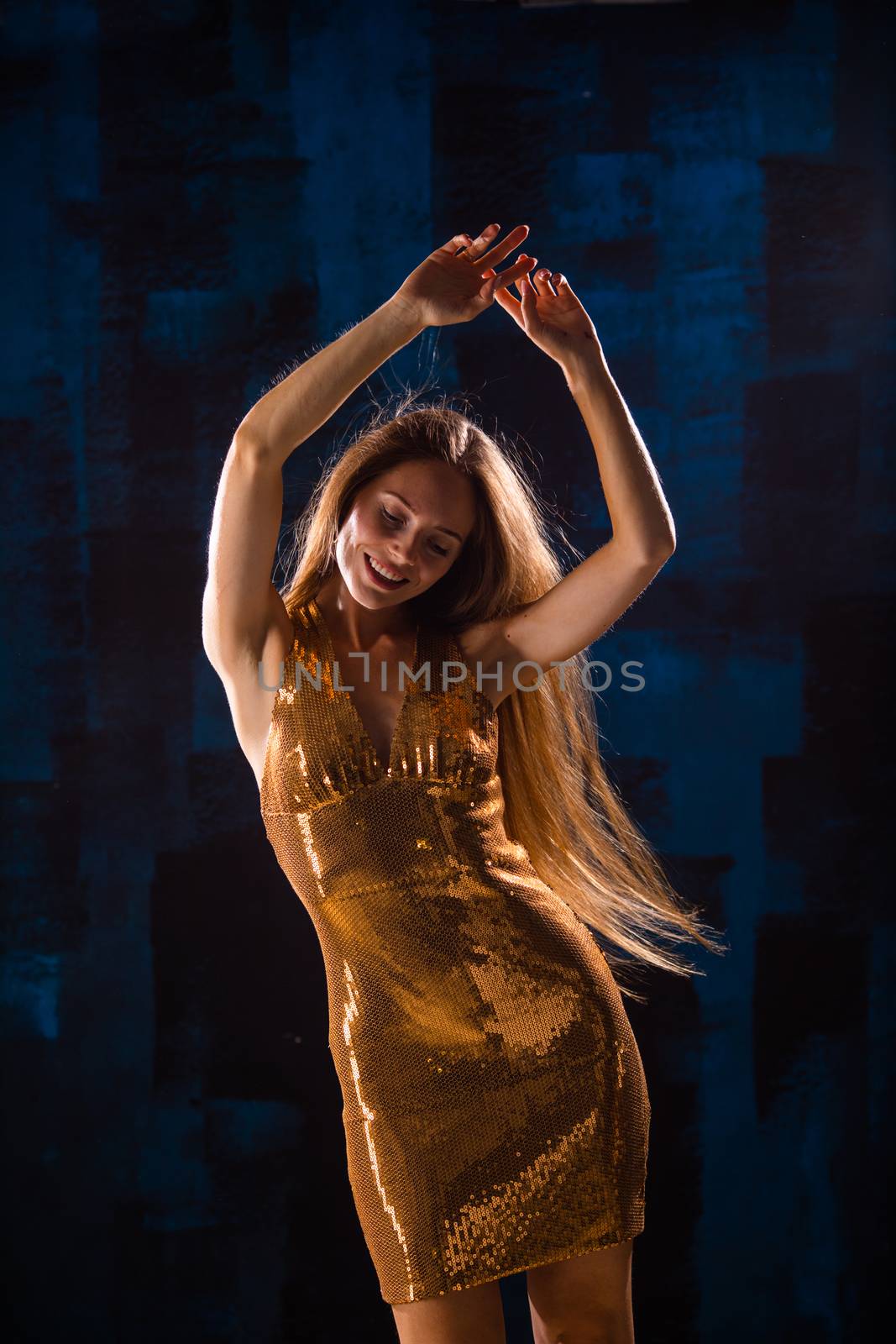 Portrait of dancing girl in golden dress on disco party blue and red studio lights