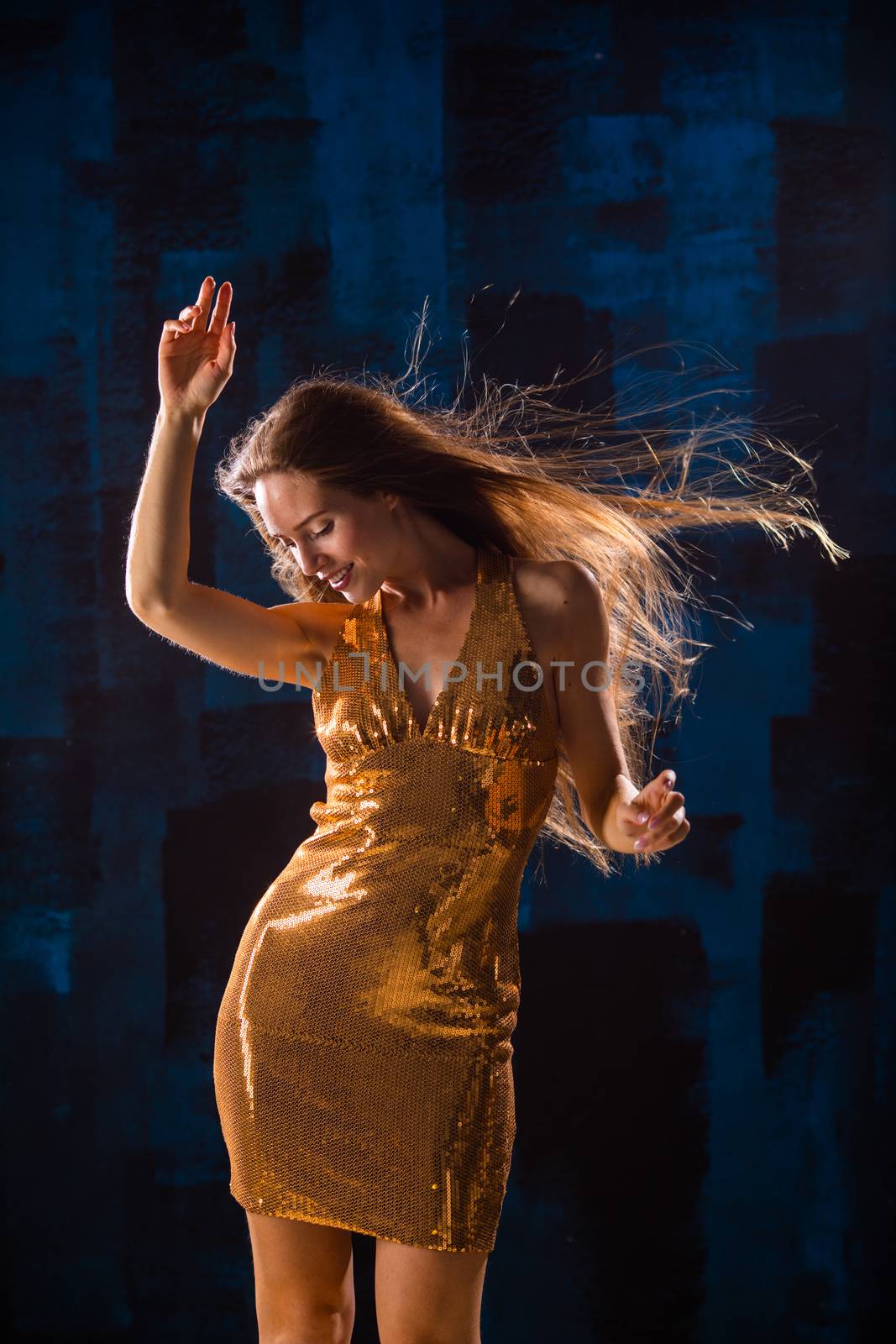 Portrait of dancing girl in golden dress on disco party blue and red studio lights