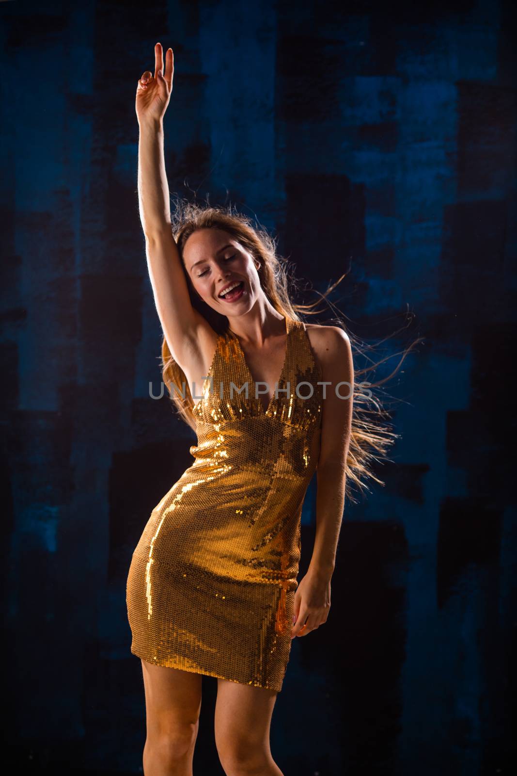 Portrait of dancing girl in golden dress on disco party blue and red studio lights