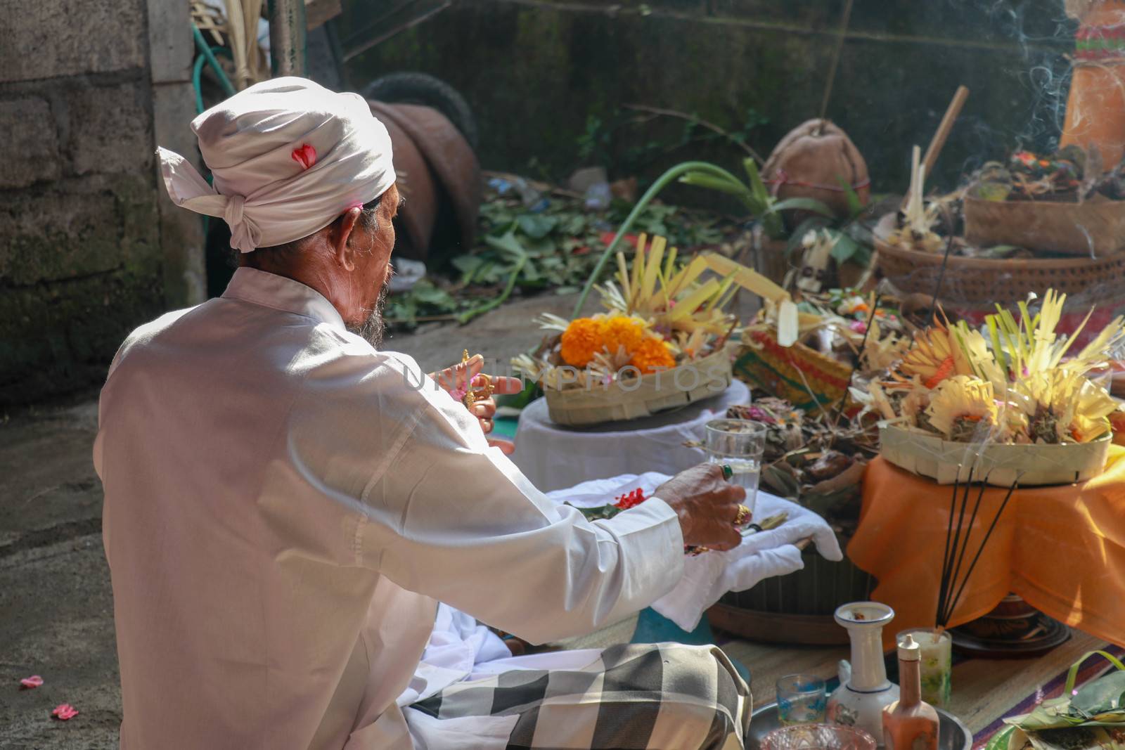 Rear view to Hindu priest praying during a wedding ceremony. Pedanda sits on the ground in front of the offerings and performs wedding ceremonies.