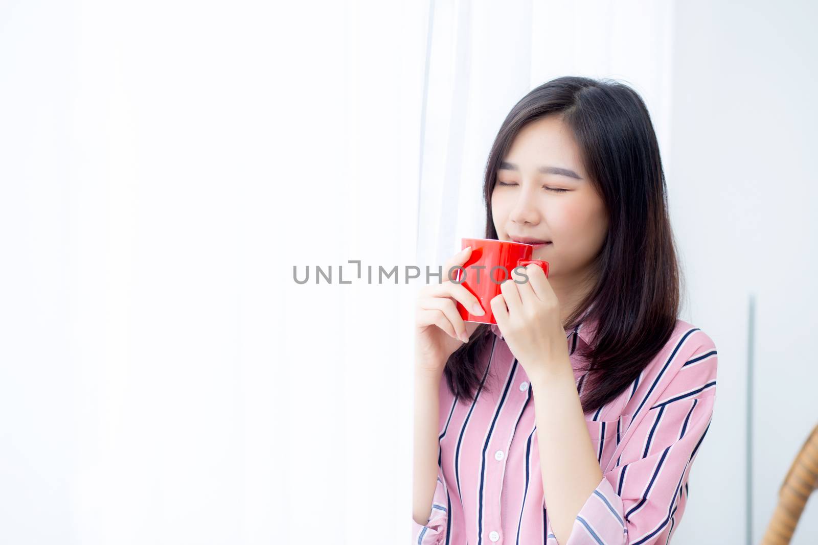 Beautiful of portrait young asian woman with drink a cup of coffee standing curtain window background in bedroom, girl relax in morning at home, lifestyle concept.