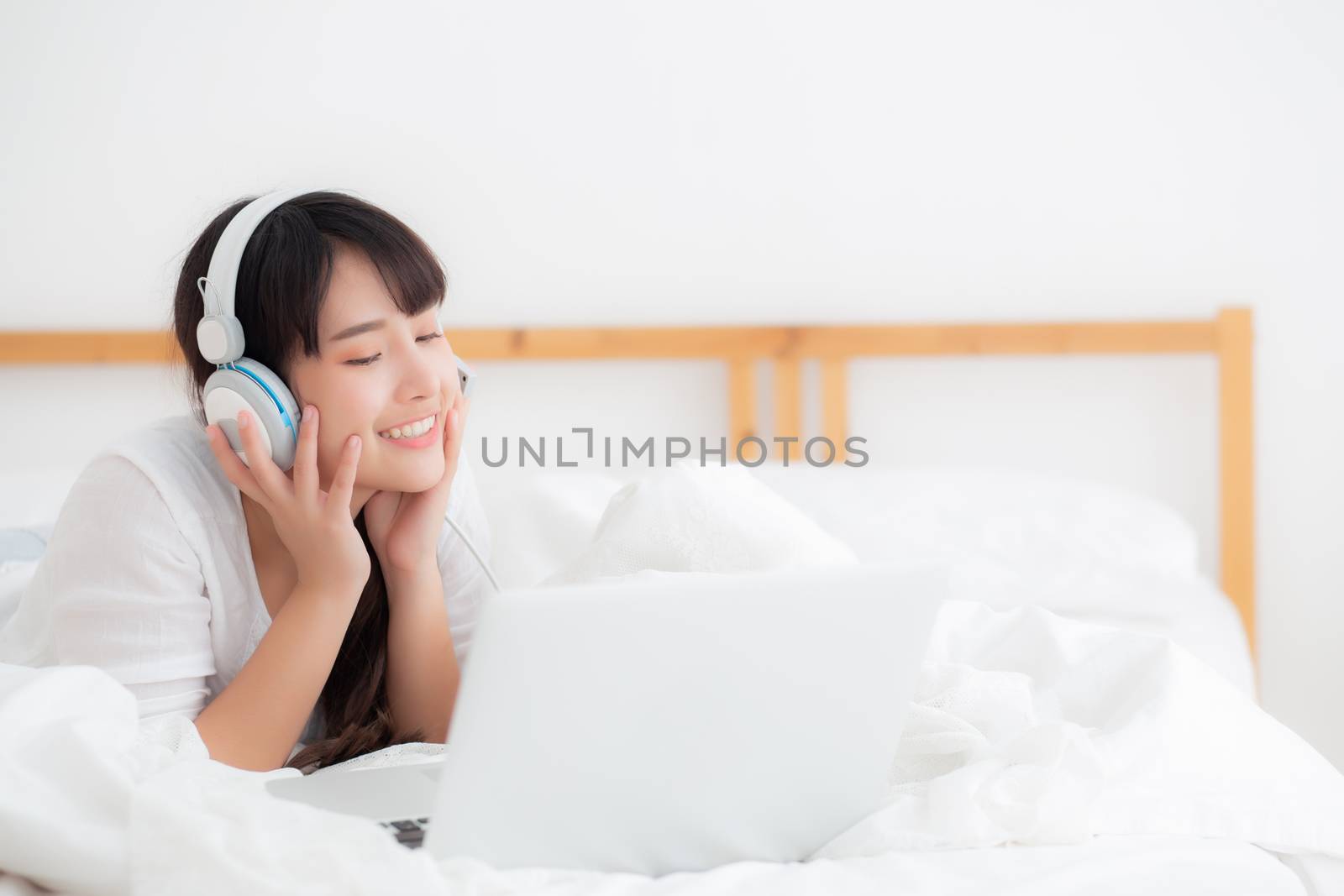 Beautiful young asia woman lying in bedroom using laptop computer showing video call chat at home, girl greet and listen and talking messenger, communication and lifestyle concept.