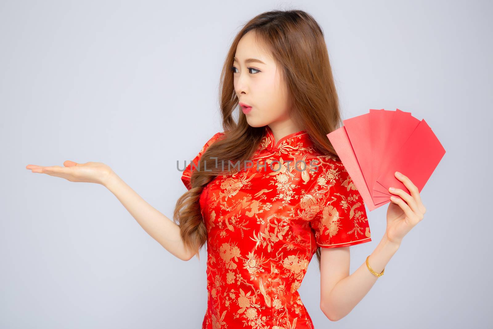Beautiful portrait asian woman cheongsam dress holding red envelope and presenting something copy space on white background, happy Chinese New Year, holiday concept.