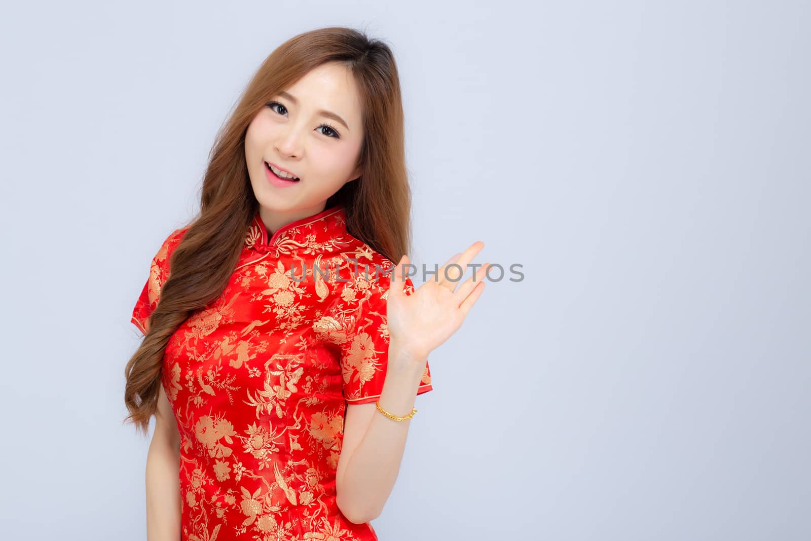Beautiful portrait happy Chinese New Year young asian woman wear cheongsam smile with gesture congratulation and greeting isolated on white background, festival and celebrate concept.