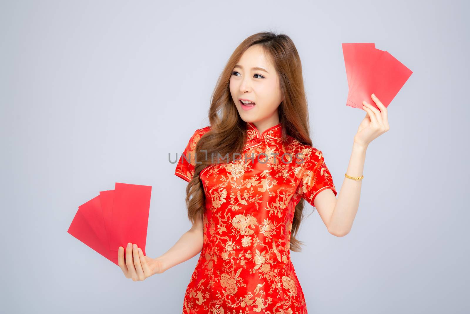 Beautiful portrait young asian woman cheongsam dress smiling holding red envelope on white background, girl celebrate with exciting, happy Chinese New Year, holiday concept.