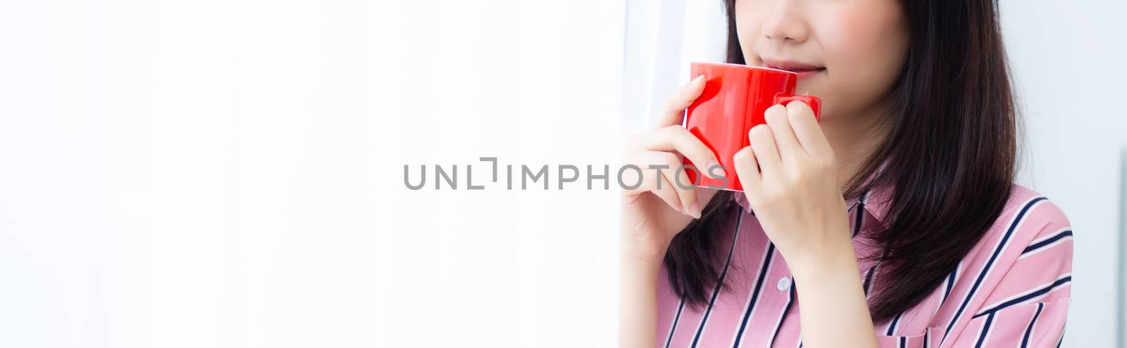 Closeup young asian woman with drink a cup of coffee standing curtain window background in bedroom, girl relax in morning at home, lifestyle concept.