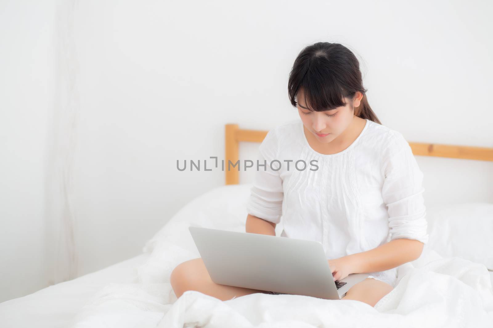 Portrait of beautiful asian young woman sitting on bed using laptop computer at bedroom for leisure and relax, freelance with girl working notebook, communication and lifestyle concept.