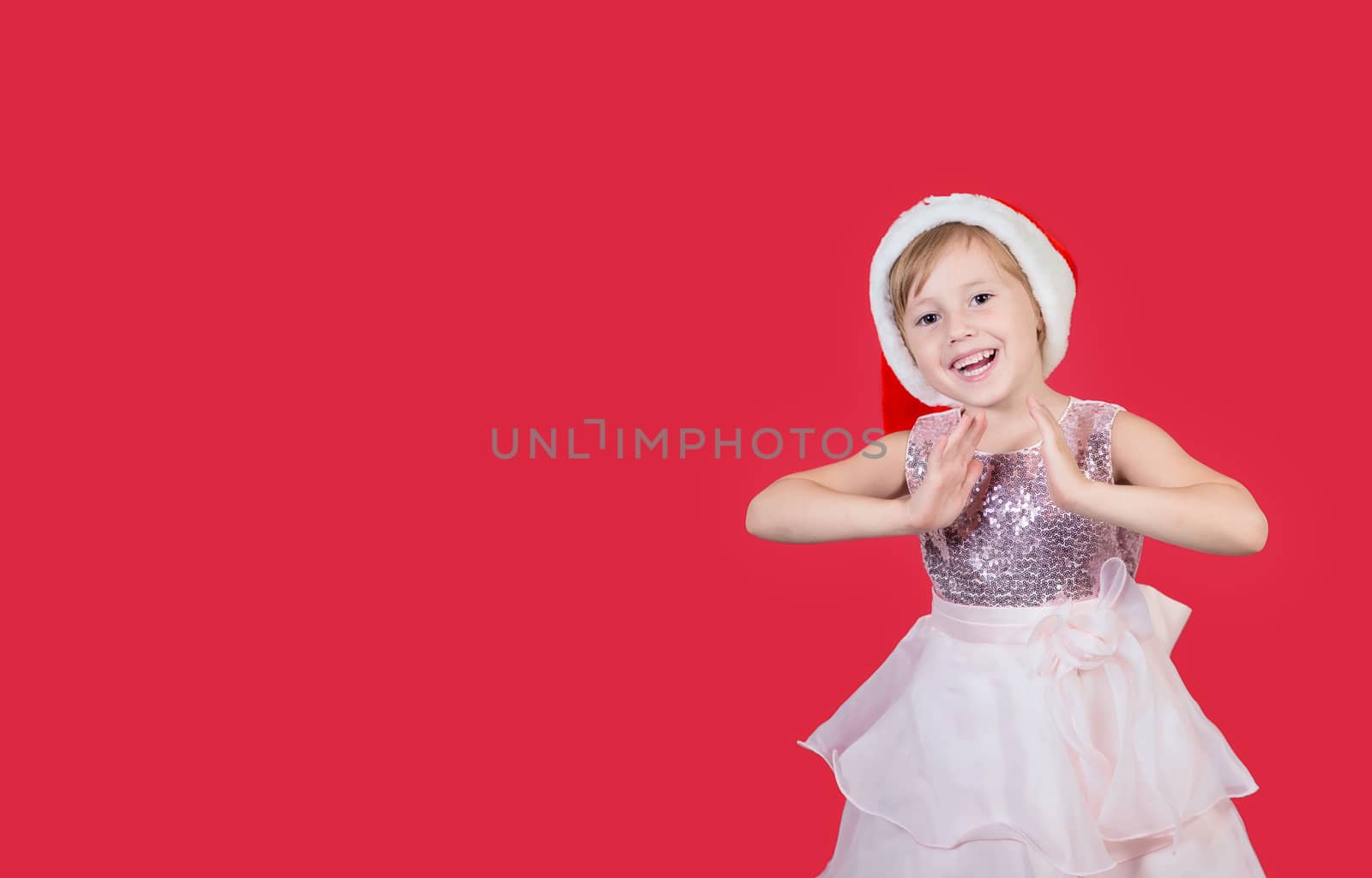 Adorable funny cacusian little girl in santa hat claps his hands for a gift celebrating happy New Year isolated on red background. Merry Christmas presents shopping sale.