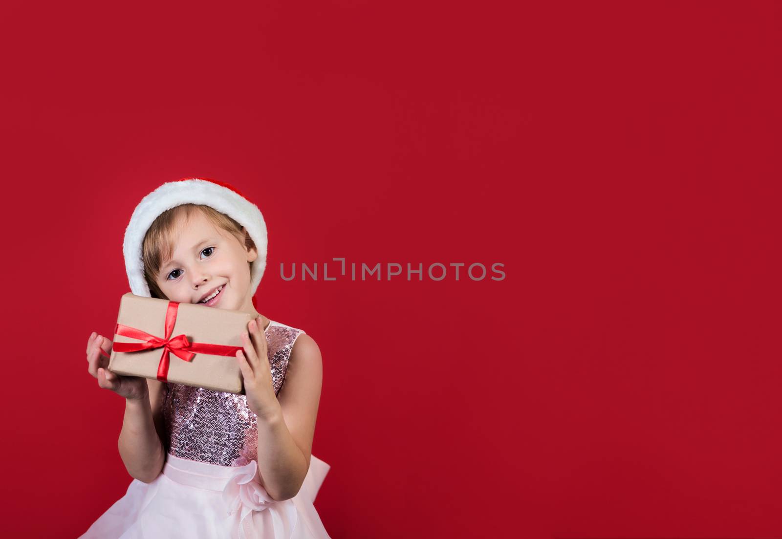 Cute adorable smiling girl holding christmas gift isolated on red by galinasharapova