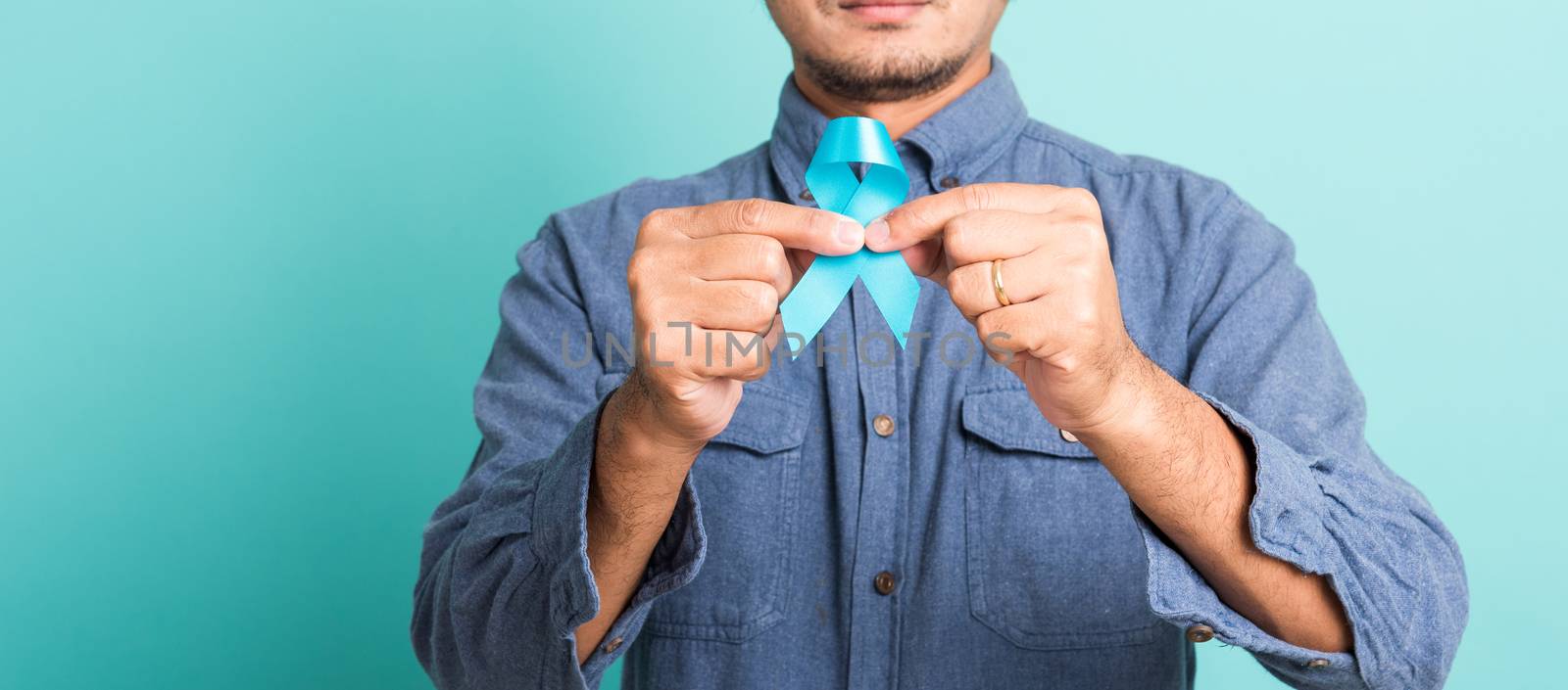 Asian portrait happy handsome man posing he holding light blue ribbon for supporting people living and illness, studio shot isolated on blue background, Prostate Cancer Awareness in November concept