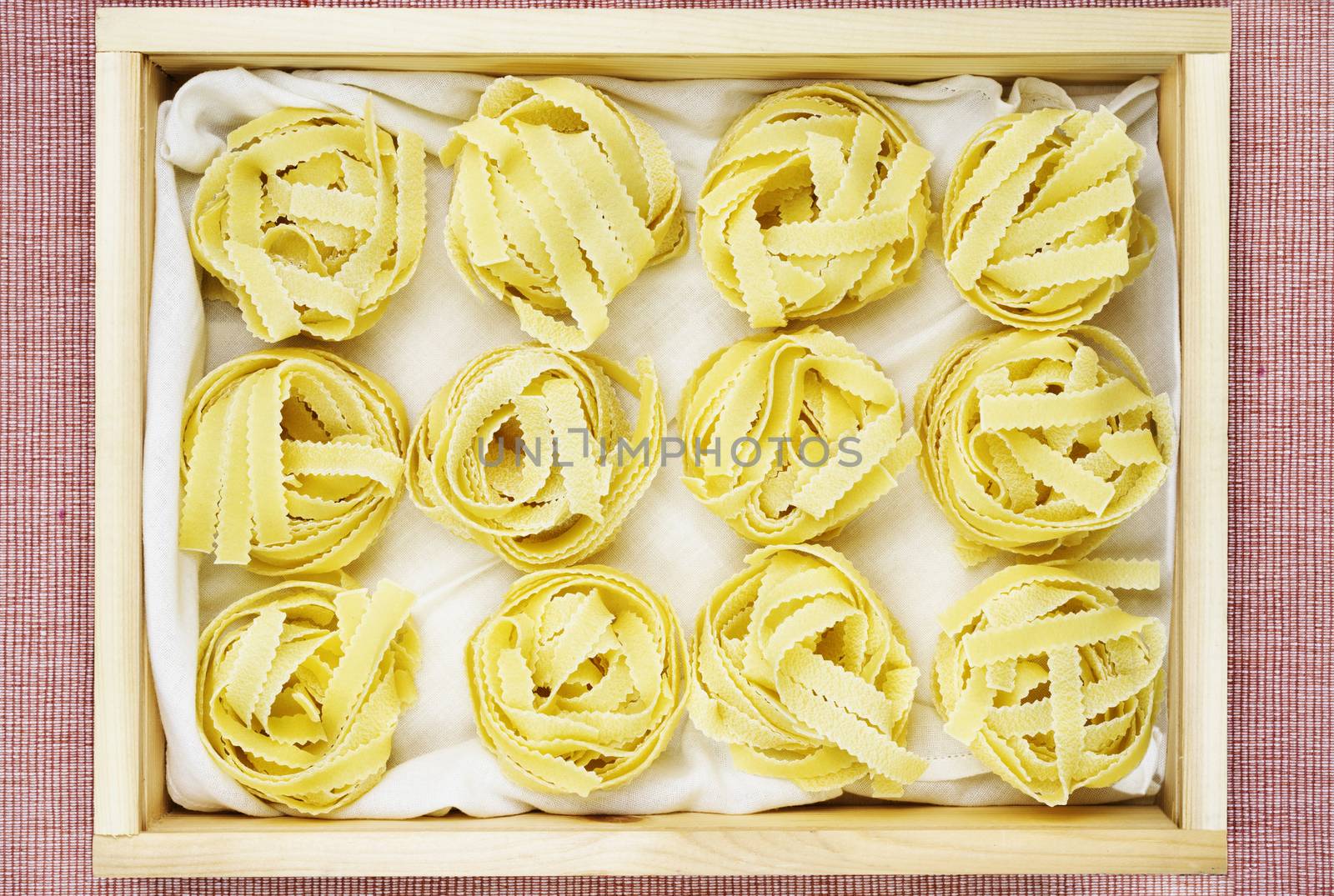 Beautiful nests of Italian pasta  fettuccine on white cotton cloth  in wooden box  , thin ribbons of pasta with geometrical edges and rough surface