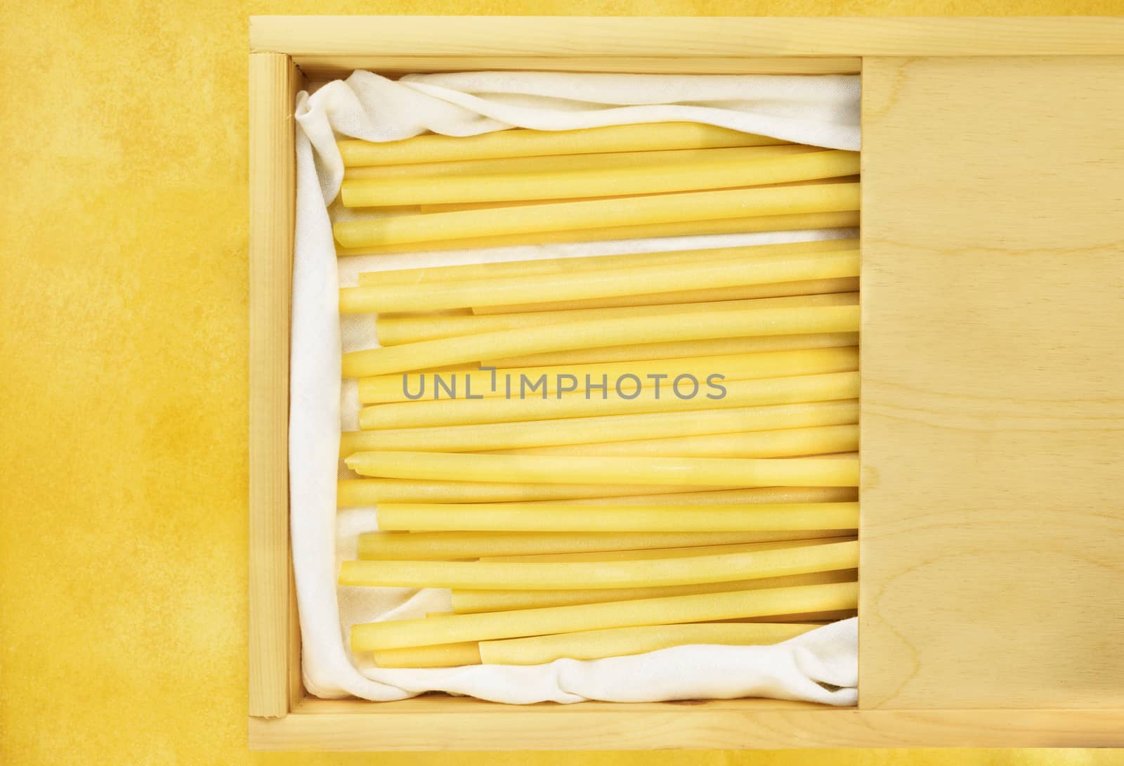 Dlicious  Italian pasta called ziti in a wooden box on yellow table ,long empty tube with smooth side 