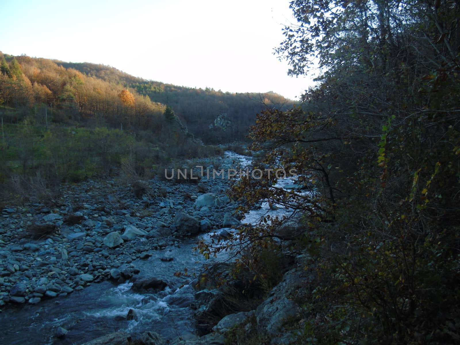 Liguria, Italy -  11/02/2020: Colorful autumn landscape around the village of Tiglieto near the city of Genova. Beautiful sunset reflection in the river and clear blue sky.