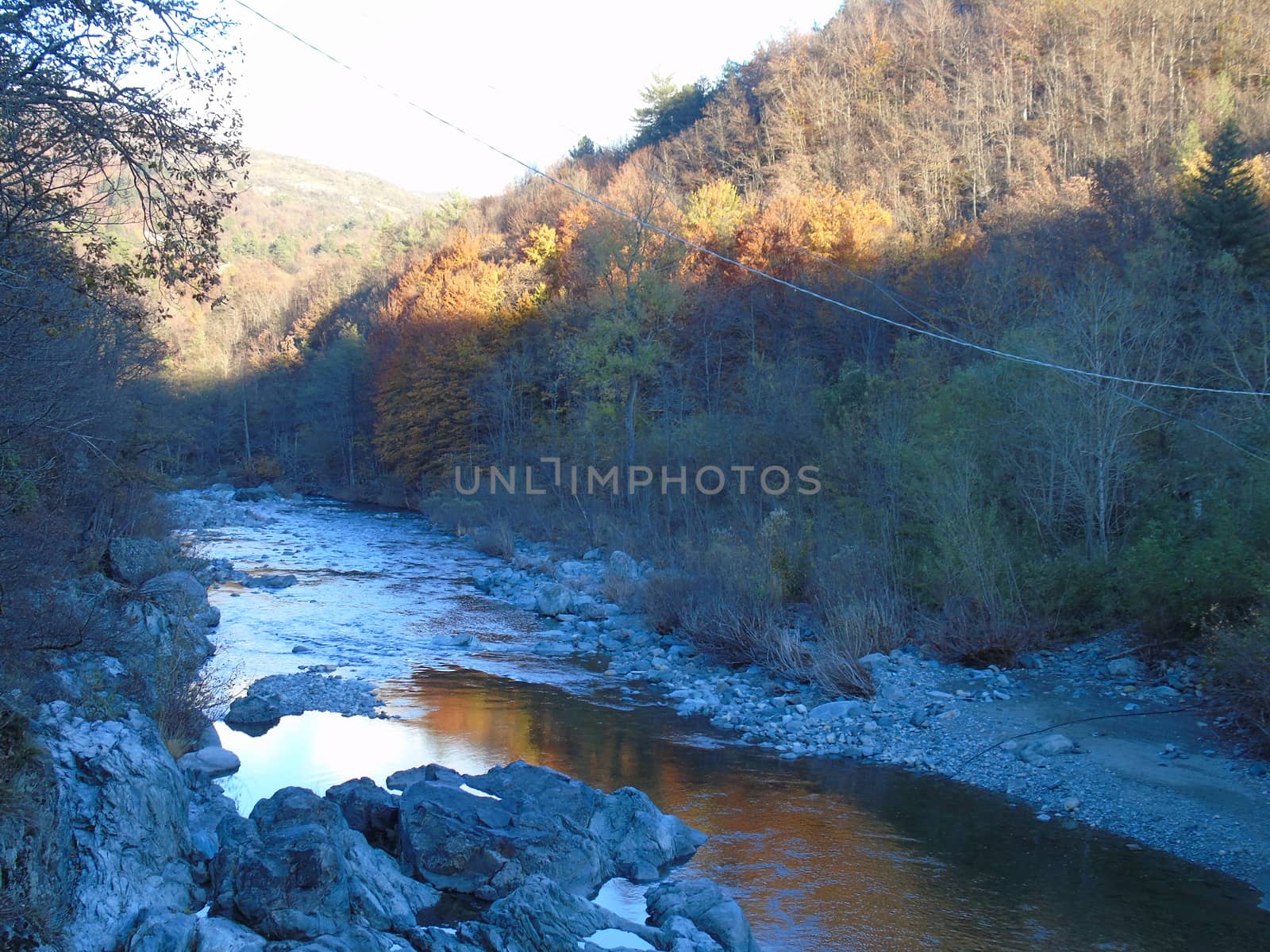 Liguria, Italy -  11/02/2020: Colorful autumn landscape around the village of Tiglieto near the city of Genova. Beautiful sunset reflection in the river and clear blue sky.