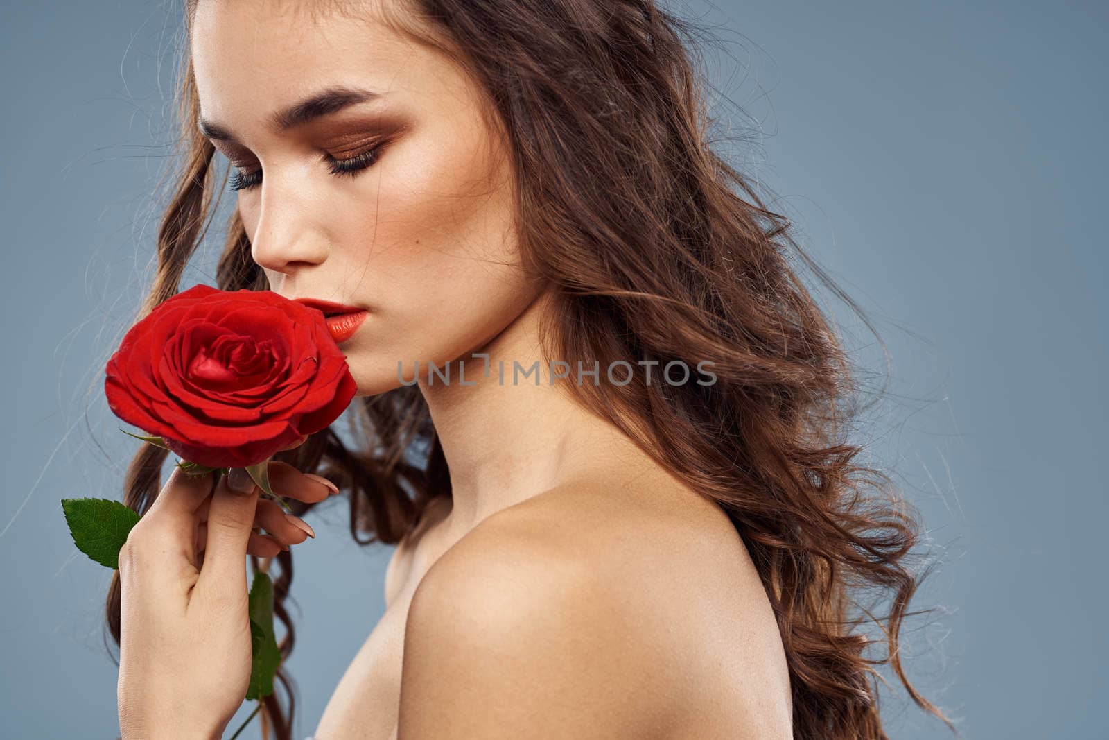 Woman portrait with red rose near the face on gray background and makeup curly hair by SHOTPRIME