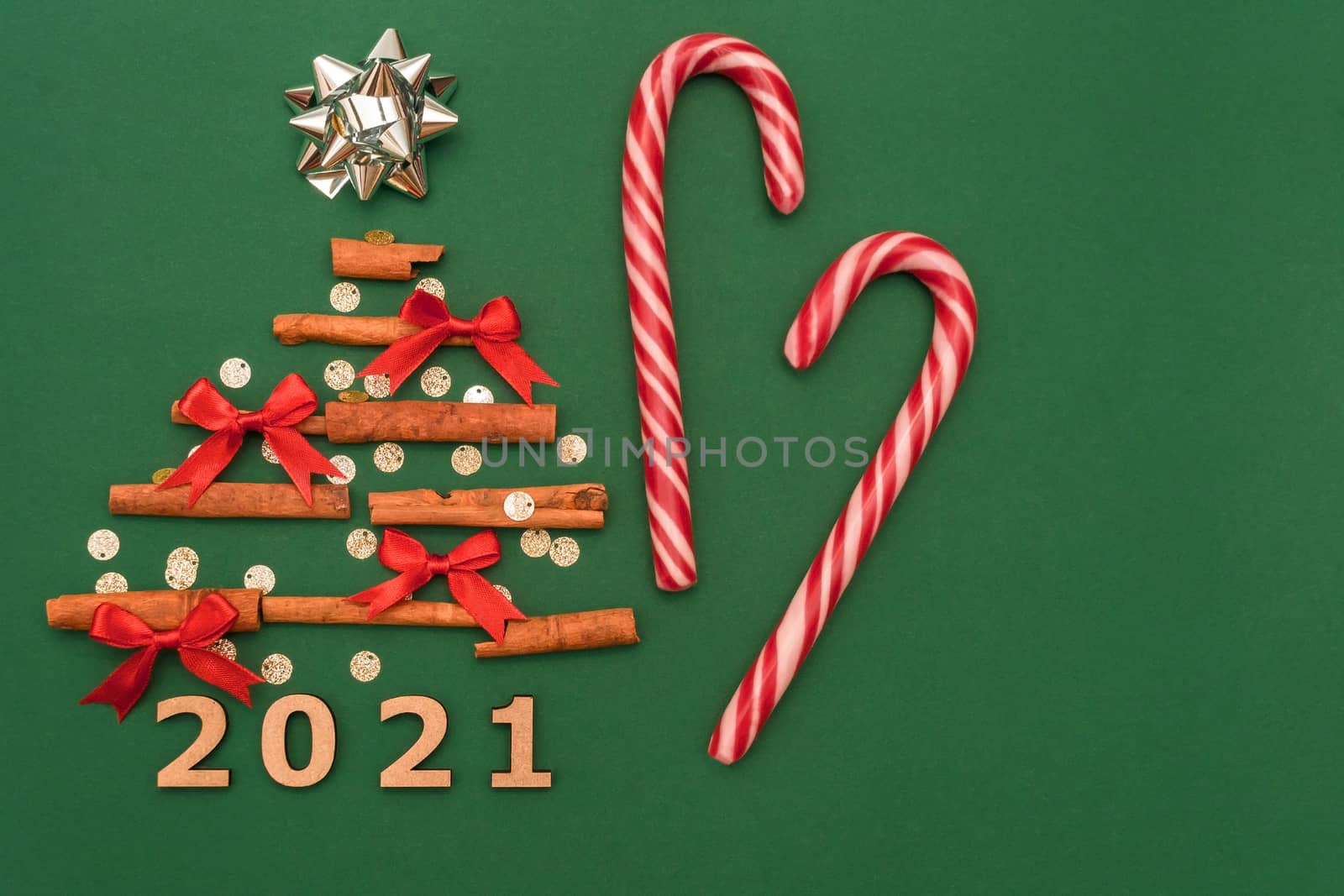 Christmas composition 2021 cinnamon tree, red bows, candy, Christmas cane candies on a green background. Christmas, winter, new year concept. Flat lay, top view, copy space by Alla_Morozova93
