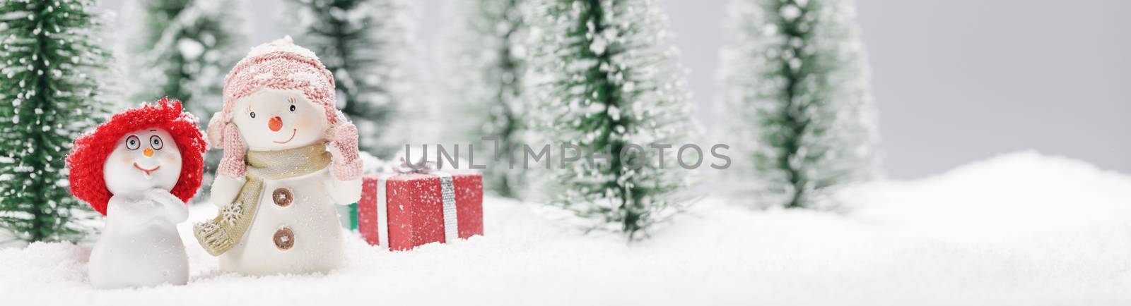 Two small cute snowmen friends with gifts in forest under falling snow