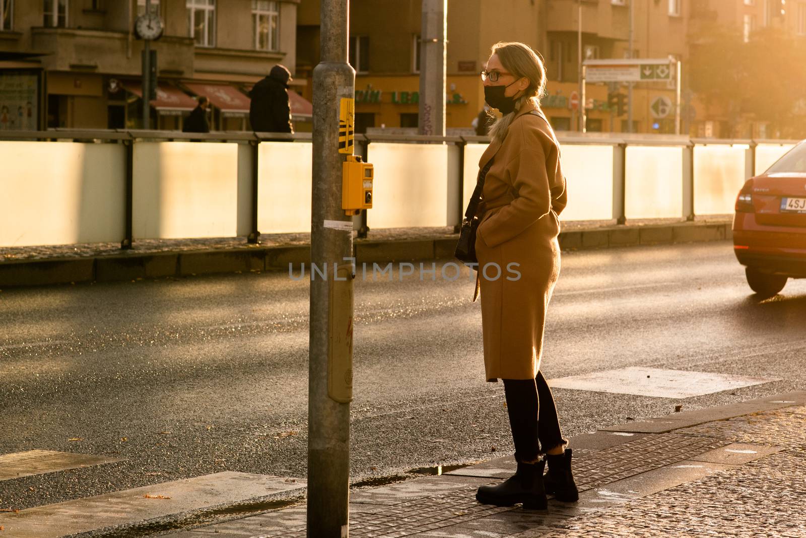 Woman with mask is waiting to cross the street at Hradcanska metro station during quarantine period due to outbreak of COVID-19 as winter is starting. Prague, Czech Republic