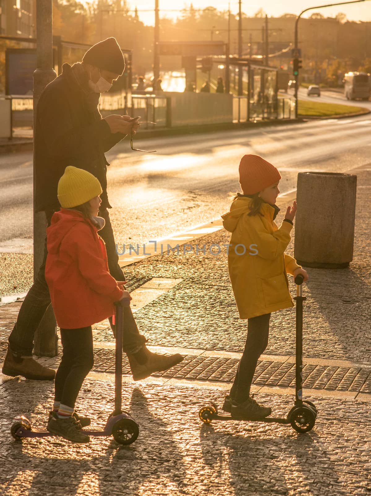 Father and two daug03/04/2018. Brno, Czech Republic. hters with mask are crossing the street at Hradcanska metro station with scooters during quarantine period due to outbreak of COVID-19 as winter is starting. Prague, Czech Republic by gonzalobell