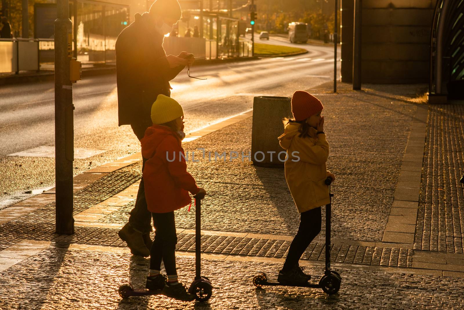 Father and two daughters with mask are crossing the street at Hradcanska metro station with scooters during quarantine period due to outbreak of COVID-19 as winter is starting. Prague, Czech Republic by gonzalobell