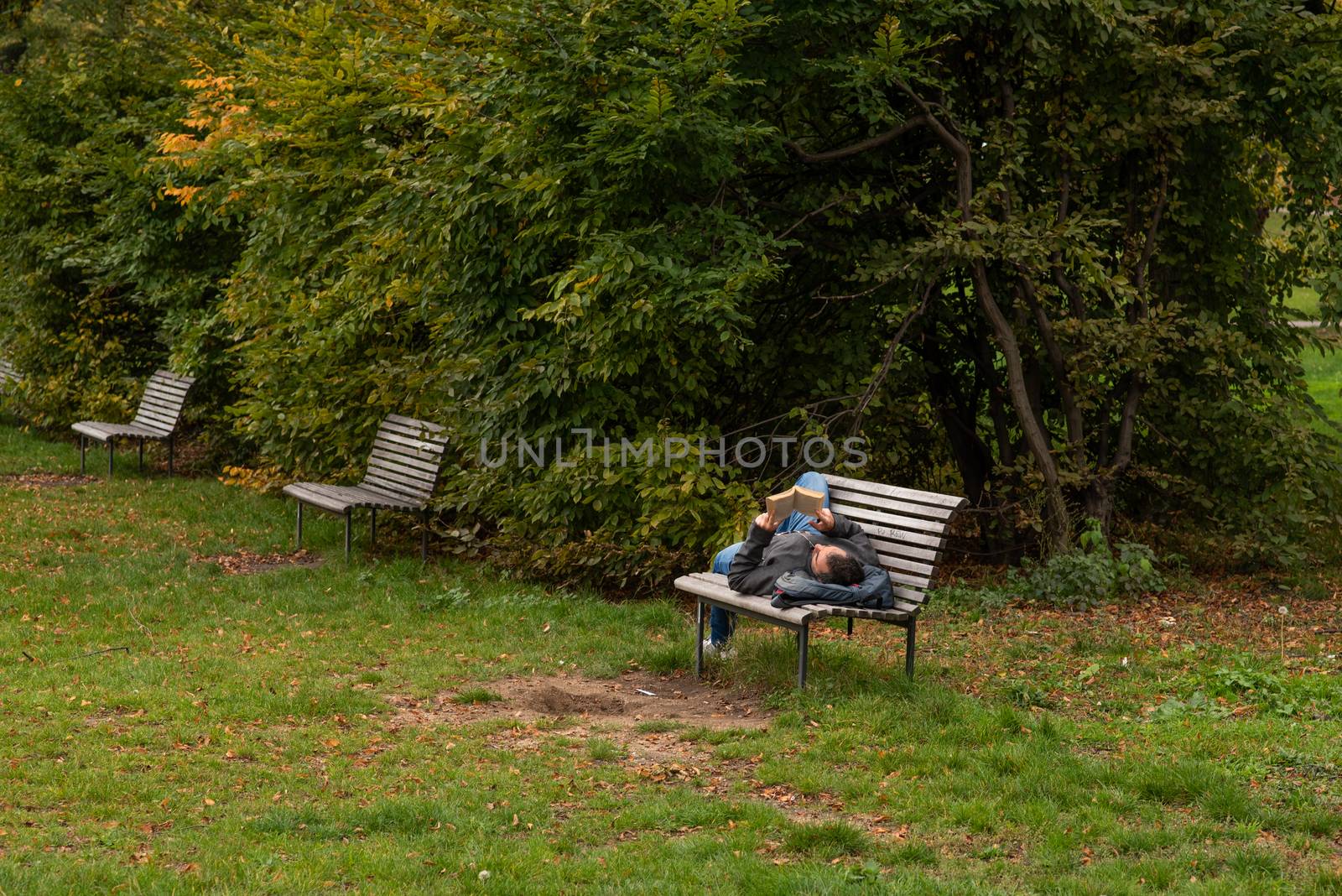 Man is laying on a bench while reading a book on Letna Park in Autumn 2020 on Prague 6during quarantine period due to outbreak of COVID-19 as winter is starting, Czech Republic