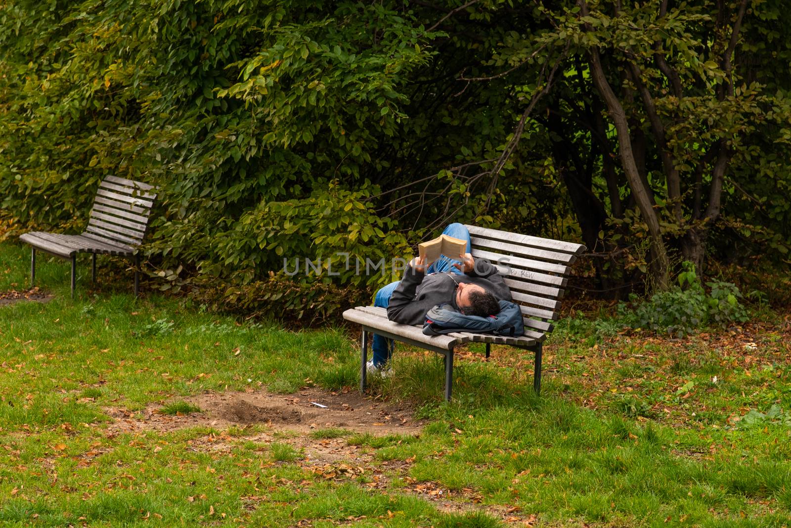 Man is laying on a bench while reading a book on Letna Park in Autumn 2020 on Prague 6 during quarantine period due to outbreak of COVID-19 as winter is starting, Czech Republic