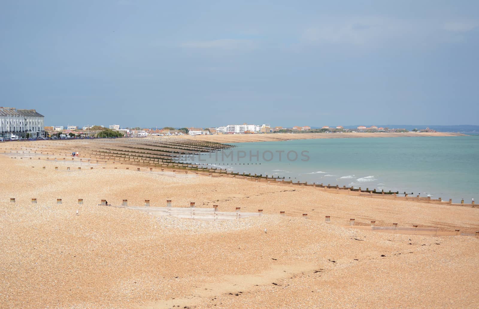 Eastbourne shingle beach in East Sussex, almost deserted on a sunny summer day. Hotels, houses and businesses line the edge of the beach.