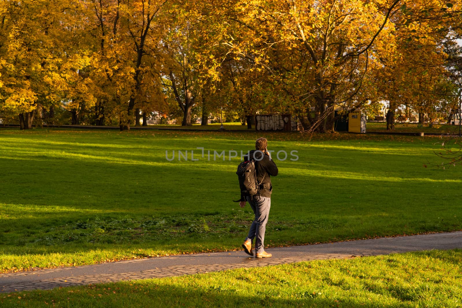 A man is speaking on a phone while walking on Park Letna in Autumn 2020 on Prague 6, during quarantine period due to outbreak of COVID-19 as winter is starting, Czech Republic by gonzalobell