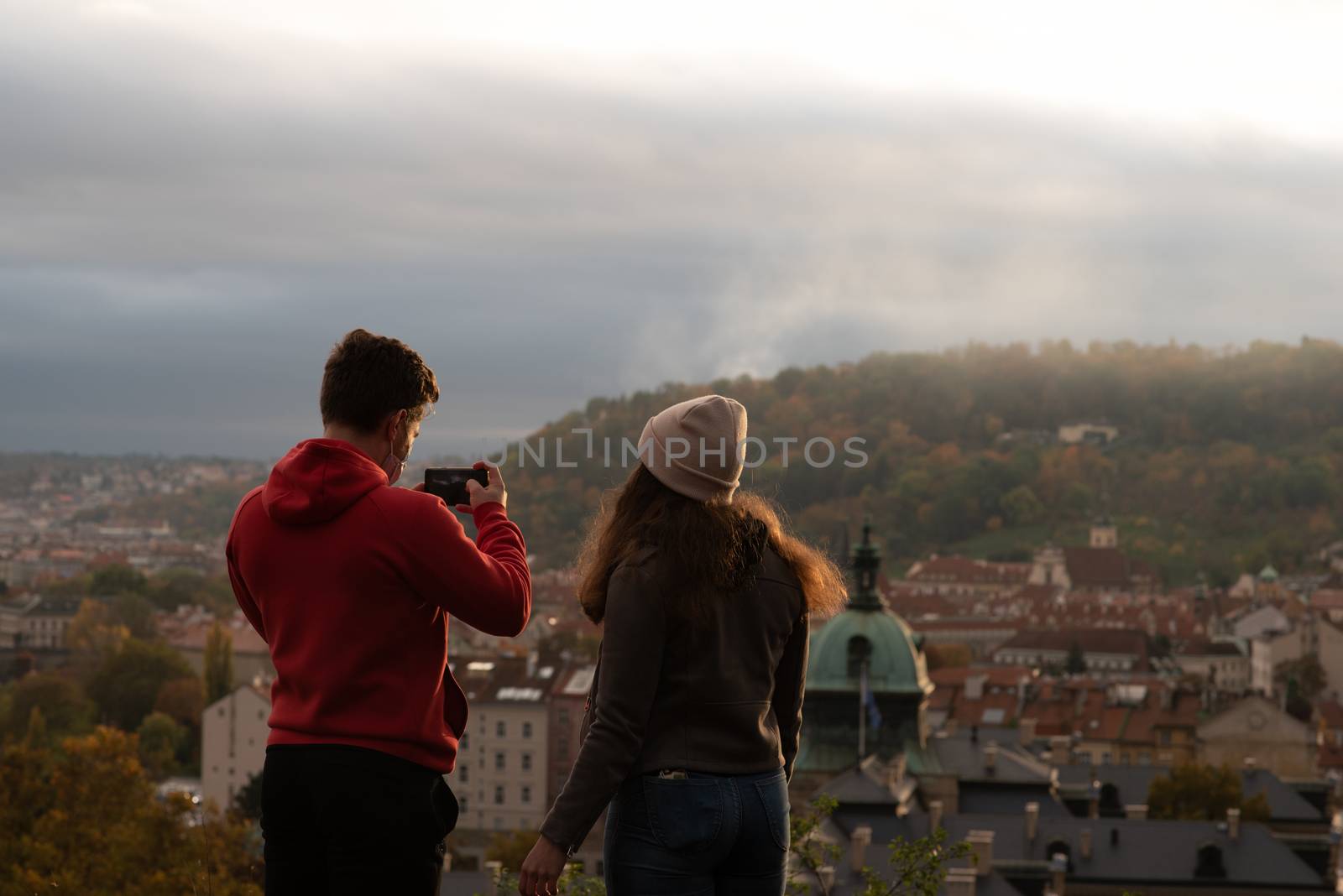 Man and woman are taking pictures and talking on Letna Park while having a spectacular view of the city center in Autumn 2020 on Prague 6, during quarantine period due to outbreak of COVID-19 as winter is starting, Czech Republic
