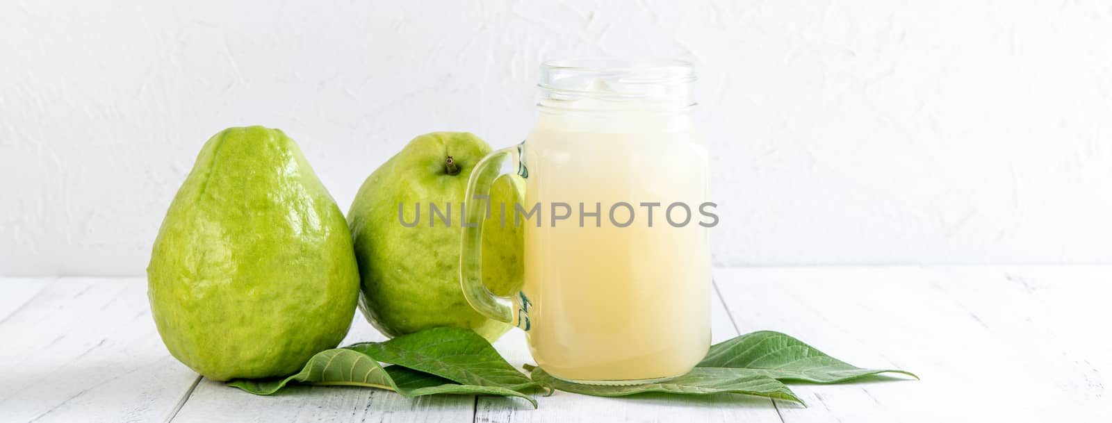 Delicious beautiful guava fruit with fresh juice set isolated on bright white wooden table background, close up.