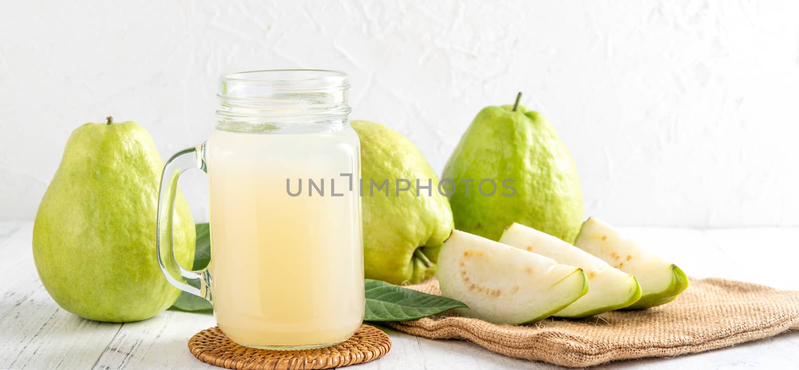 Delicious beautiful guava fruit with fresh juice set isolated on bright white wooden table background, close up.