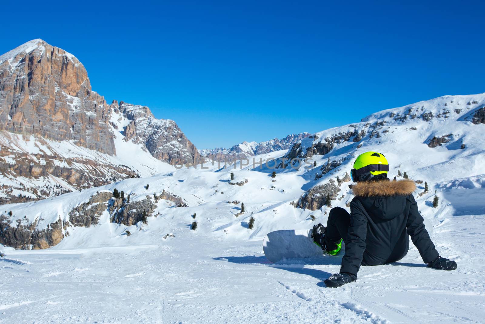 Rear view of female snowboarder sitting on ski slope at resort in Dolomites Italian Alps